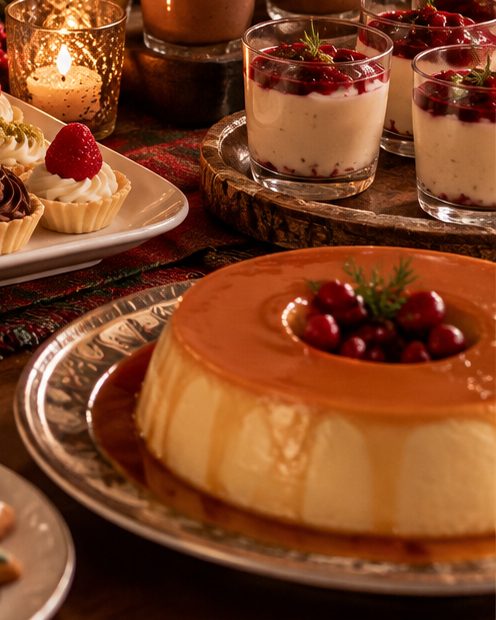 Pudim com calda de caramelo e frutas vermelhas, ao lado de taças de sobremesa