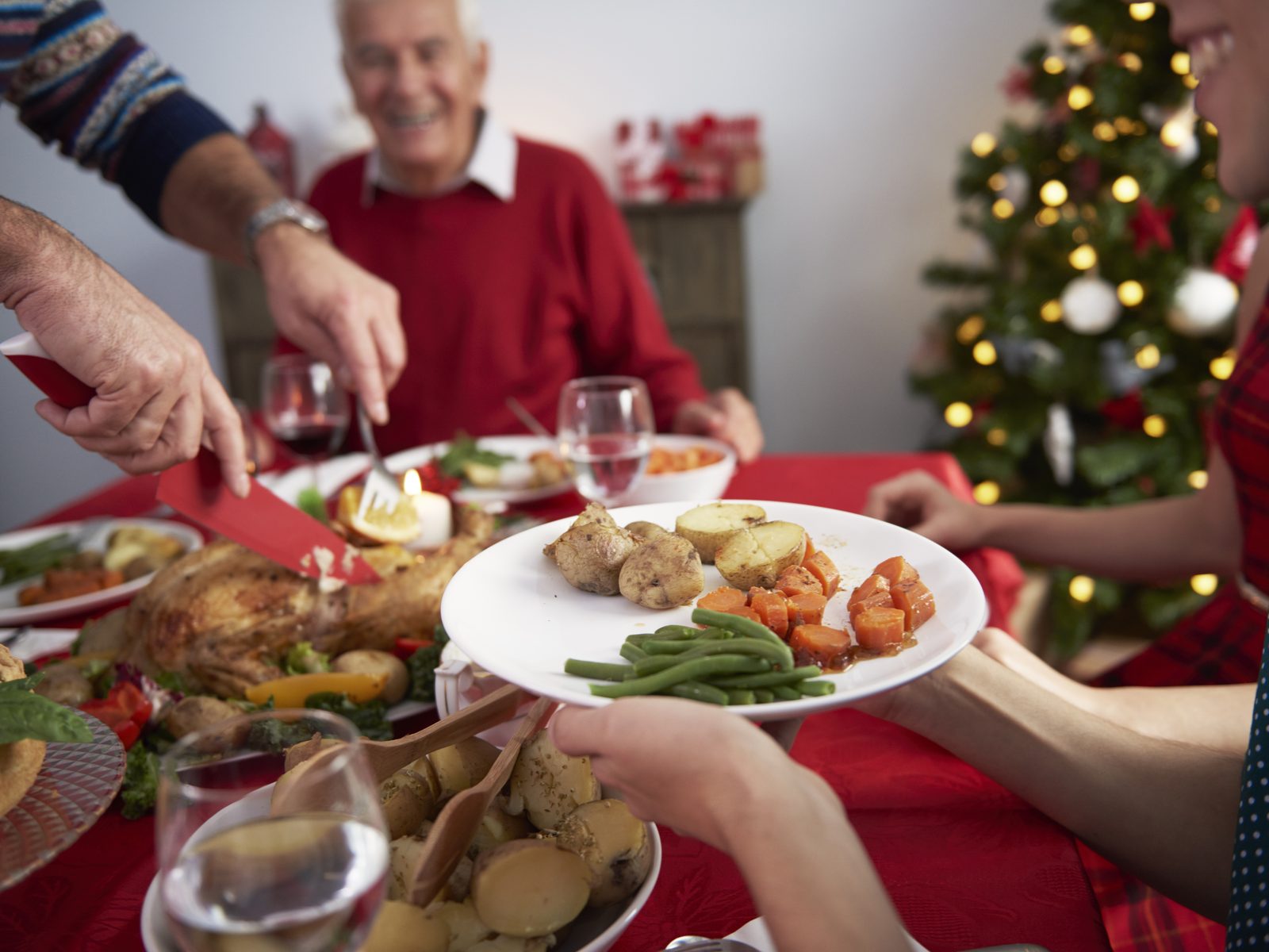 Família à mesa enquanto o peru de Natal é cortado e servido com batatas, vagem e cenoura